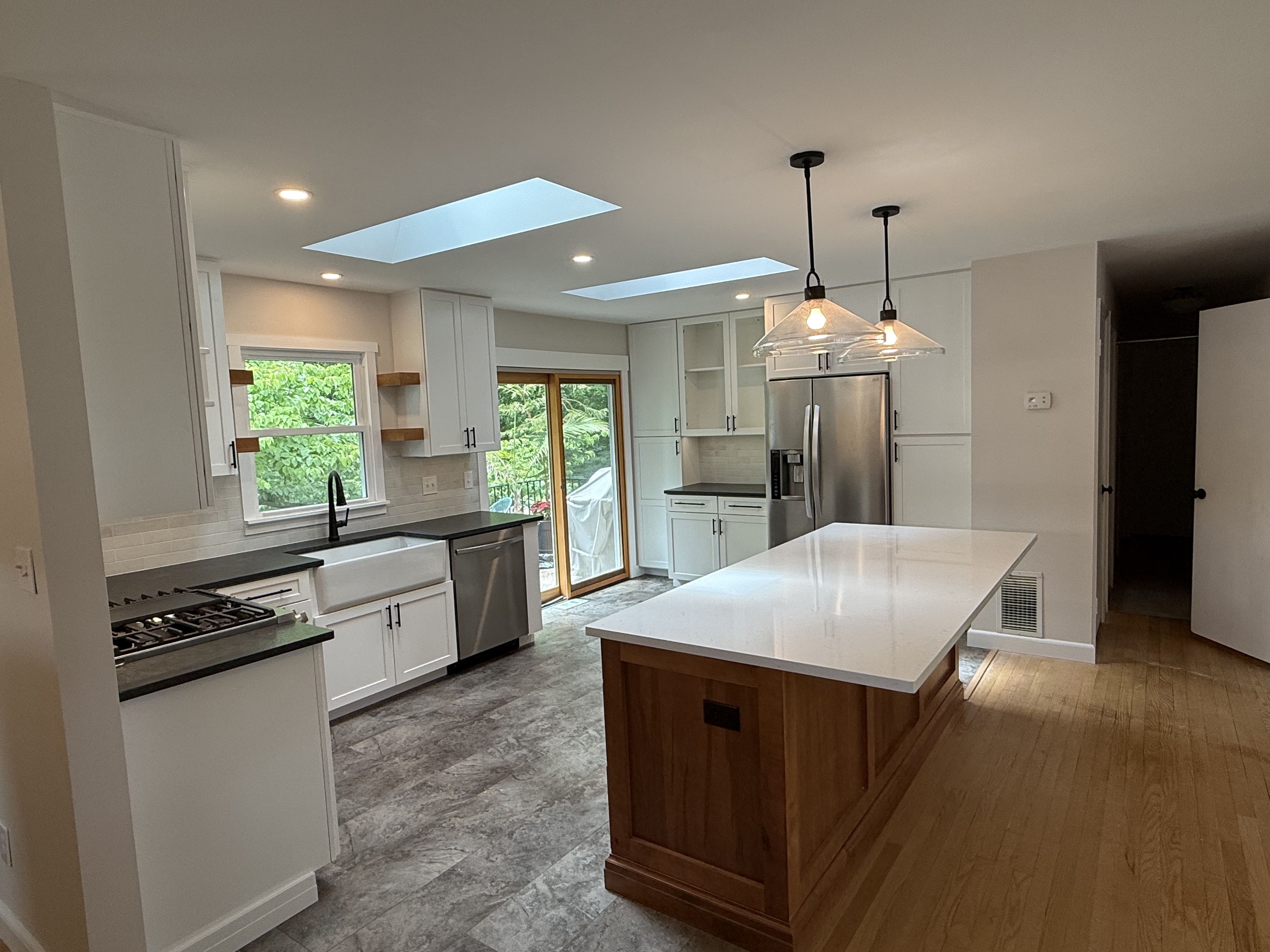 Modern kitchen remodel featuring white shaker cabinets, stainless steel appliances, quartz island countertop, farmhouse sink, and pendant lighting with natural wood accents.